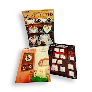 May include: Three instructional craft booklets featuring embroidery patterns. The top booklet is titled Holiday Bread Cloths. The bottom left booklet is titled A Regal Rose and a distinctive floral alphabet. The bottom right is Oriental Influence.