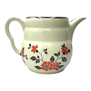 May include: A cream-colored ceramic pitcher with a rounded, ribbed body and a curved handle. The surface is decorated with a repeating pattern of vibrant orange flowers and dark black leaves, featuring a wide spout and a metallic-toned rim.