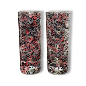 May include: Two clear glass shot glasses featuring a chaotic, abstract pattern of thin black and red lines. The text "TEQUILA ROSE" is printed in black on the front of each glass. The glasses have a cylindrical shape with a thick, solid base.