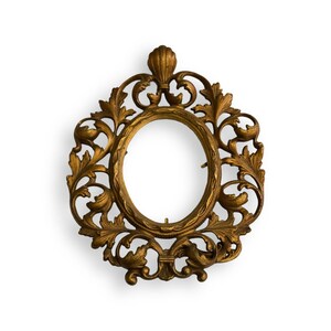 May include: An oval-shaped gold-colored picture frame featuring an intricate openwork design of scrolling acanthus leaves and vines. The top of the frame is accented with a prominent shell motif, and the metal surface displays a textured finish.