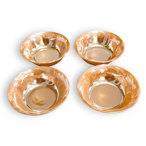 May include: Four iridescent orange-colored bowls with a leaf design around the rim. The bowls have a rounded shape and a smooth, reflective surface. The bowls are arranged in a square formation against a white background.