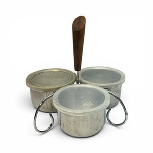 May include: A stainless steel condiment server with three round containers, each with a clear lid. A dark wooden handle rises from the center. The containers are held in place by a curved metal frame.