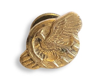 May include: A vintage gold-toned lapel pin featuring an eagle with outstretched wings, a shield, and a circular border. The pin has a classic design and a textured surface, suggesting it is an antique or collectible item.