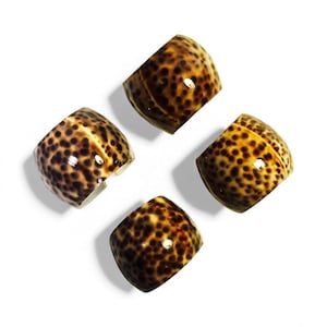 May include: Four decorative, open-ended rings with a spotted pattern in shades of brown and tan. The rings are arranged in a square shape against a white background. The rings appear to be made of a glossy material.