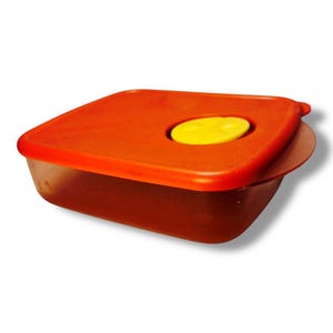 May include: An orange plastic food storage container with a matching lid. The lid has a yellow, oval-shaped button in the center. The container is square with rounded corners.
