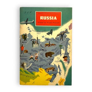 May include: A vintage softcover book titled RUSSIA Around the World Program by the American Geographical Society. The green and yellow cover features a map of Russia with illustrations of a plane, a bear, a tiger, a seal, and people in traditional clothing.