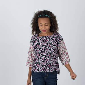 Puede incluir: Una persona joven con una blusa de estampado floral de manga larga y pantalones vaqueros azules. Lleva botas de vaquero marrones con costuras decorativas.