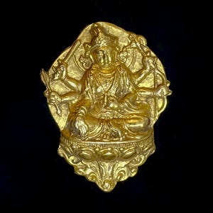 May include: A gold-colored statue of a seated deity with multiple arms, holding various objects. The statue is set against a black background. The deity is adorned with detailed ornamentation, including a crown and jewelry. The overall design suggests a religious or spiritual theme.