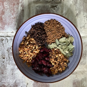 Puede incluir: Un cuenco azul claro lleno de varios ingredientes secos, incluyendo clavos, ar&aacute;ndanos y hojas de laurel. El cuenco est&aacute; sobre un fondo de pared de ladrillo texturizado. Los ingredientes est&aacute;n dispuestos en secciones.