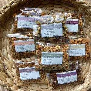 May include: A woven basket filled with several clear plastic pouches of stovetop simmering potpourri. Each pouch has a label with the name of the scent, such as "Cranberry Orange" and "Pumpkin Latte". The potpourri includes dried herbs, spices, and fruit.