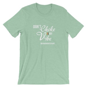 May include: A light green t-shirt with the text "Don't Choke My Vibe" in white. The text is in a stylized font with a colorful flag graphic. The text "III GUARDWHATSYOURS" is below the main text.