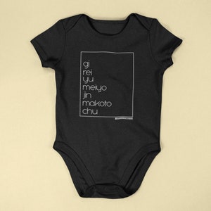 May include: Black baby bodysuit with white text inside a white rectangle. The text reads "gi, rei, yu, meiyo, jin, makoto, chu". The bodysuit has short sleeves and a snap closure.