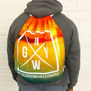 May include: A drawstring bag with a sunset and ocean scene. The bag has a white logo with the text "GUARDWHATSYOURS" and the letters "GWY" in a white circle.