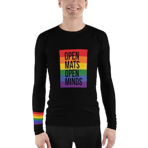 Puede incluir: Camiseta negra de manga larga con una franja arcoíris en la manga y un rectángulo de colores arcoíris en la parte delantera con el texto "OPEN MATS OPEN MINDS" en negro.