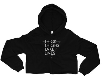 May include: Black cropped hoodie with a white triangle graphic and the text "THICK THIGHS TAKE LIVES" inside the triangle.