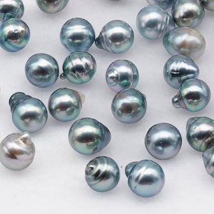 Peut inclure: Une collection de perles de Tahiti bleu-gris irisées, chacune avec une forme et une taille uniques. Les perles sont éparpillées sur une surface blanche.