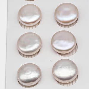 May include: Six lustrous, off-white, coin-shaped pearls are arranged in a grid within a white display. The pearls have a smooth, iridescent surface, reflecting light with a soft glow. The pearls are likely used for jewelry making.