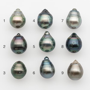 Peut inclure: Neuf perles irisées en forme de goutte d'eau de tailles et de couleurs variées sont présentées sur un fond blanc. Les perles présentent une gamme de teintes, dont le vert, le bleu et le violet, avec une surface brillante et réfléchissante. Chaque perle a une forme unique.