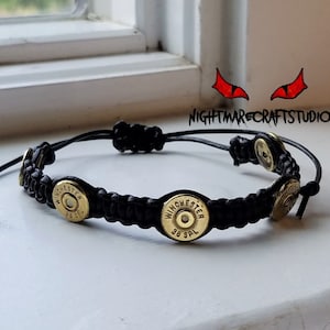 May include: Black paracord bracelet with four gold-colored bullet casings. The casings are engraved with "Winchester 38 SPL".