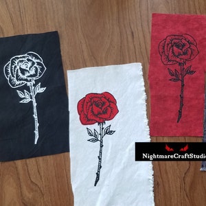 Peut inclure: Quatre carrés de tissu avec des roses noires et rouges brodées. Les roses sont bordées de noir et ont une tige avec des épines. Les carrés de tissu sont noirs, blancs, rouges et gris.