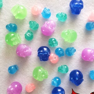 May include: A collection of small, translucent skull-shaped beads in various colors including blue, green, pink, and light blue. Some beads feature glitter accents. The text NIGHTMARECRAFTSTUDIO is printed in the bottom right corner.