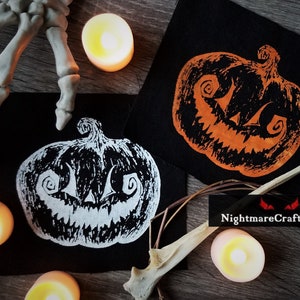 May include: Two black fabric patches with white and orange embroidered jack-o'-lantern faces. The patches are surrounded by candles, a skeleton hand, and a twig. The text "NightmareCraftStudio" is visible in the bottom right corner.