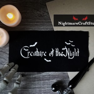 May include: Black fabric patch with white embroidery that reads "Creature of the Night" with stylized bats above and below the text.