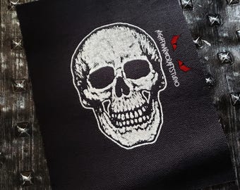 May include: A black patch featuring a detailed white skull design. The skull has visible teeth and eye sockets. The text "NIGHTMARECRAFTSTUDIO" is printed on the right side of the patch in white.