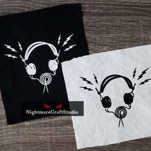 May include: Two black and white fabric patches featuring an image of headphones with lightning bolts emanating from them. The text "NightmareCraftStudio" is at the bottom of the black patch.