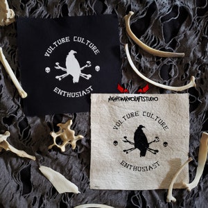 May include: Two embroidered patches featuring a black and white vulture design. The patches are displayed on a dark grey fabric background with white bones scattered around them. The text on the patches reads "Vulture Culture Enthusiast".