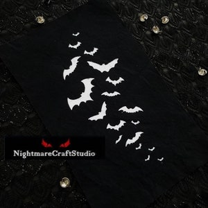 May include: Black fabric patch with a white embroidered design of bats flying in a diagonal line. The patch has the text "NightmareCraftStudio" in red letters.