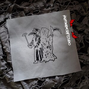 May include: Black and white embroidered patch featuring a plague doctor holding a staff with a flower on top, and a skeletal figure behind them. The patch has the text "NIGHTMARECRAFTSSTUDIO" in white on a black background.