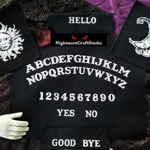 May include: A set of black iron-on patches featuring a sun, moon, and a Ouija board with the words "HELLO", "GOOD BYE", "YES", "NO", and "NightmareCraftStudio".