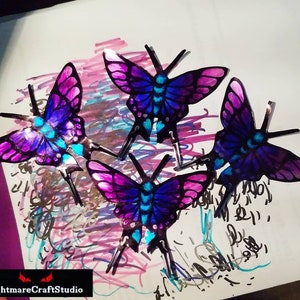 May include: Four iridescent butterflies with purple, blue, and pink wings. The butterflies are arranged in a cluster on a white background with colorful scribbles.