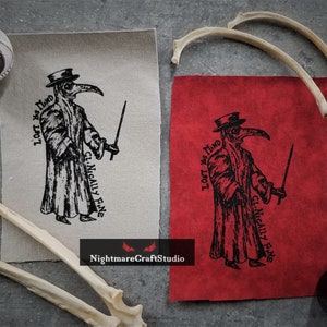 May include: Two fabric patches with a black and white illustration of a plague doctor holding a staff. The text on the patches reads "Lest We  Find" and "Clinically Fine".