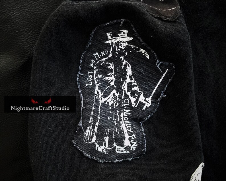 May include: Black and white embroidered patch of a plague doctor wearing a long coat, hat, and mask. The text "LOST HIS MIND" is on the left side of the patch and "CLINICALLY FINE" is on the right side.