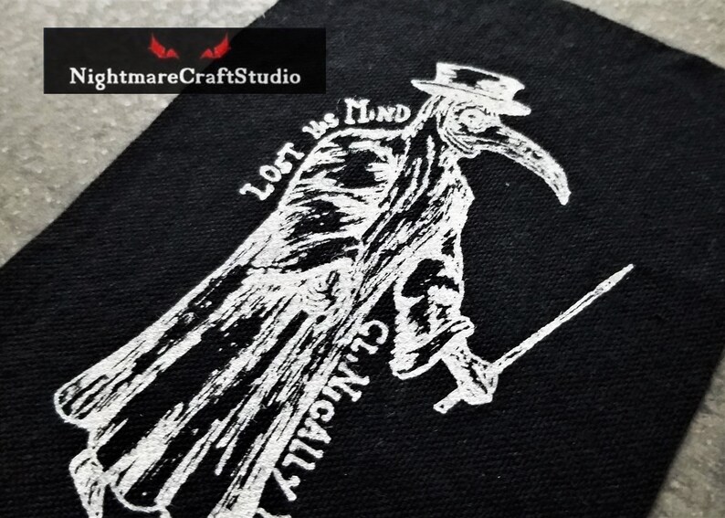 May include: Black and white embroidered patch featuring a plague doctor with a long beak and a hat. The text "Lost in the Mind" is written above the doctor.