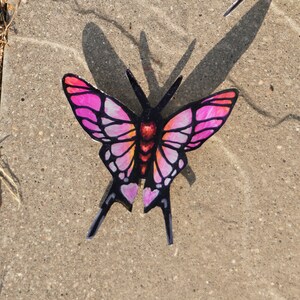 May include: A pink and black butterfly with a heart-shaped design on its wings. The butterfly is made of paper and has a 3D effect.