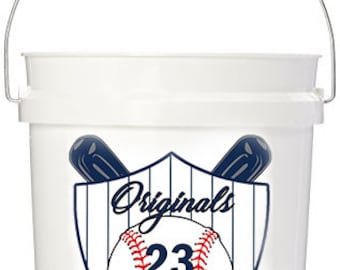 Może przedstawiać: Biały plastikowy kubeł z srebrnym uchwytem. Kubeł ma projekt w stylu baseballowym z piłką baseballową, kijami i tekstem "Originals 23 Sebastian".