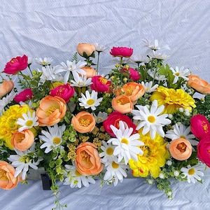 May include: A vibrant floral arrangement featuring a mix of colorful blooms. The bouquet includes bright pink, yellow, orange, and white flowers, with green foliage. The flowers are arranged on a white background.