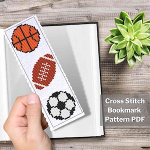 May include: A white bookmark with a cross stitch pattern of a basketball, football, and soccer ball. The bookmark is on a book with the text "Cross Stitch Bookmark Pattern PDF".