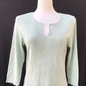 May include: A light green, long-sleeved shirt with a V-neck and a scalloped hem.