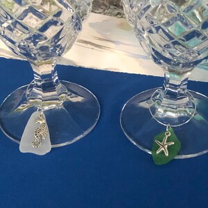 May include: Two clear glass wine glasses with decorative seahorse and starfish charms hanging from the stems. The glasses are on a blue surface.