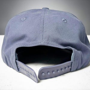 Custom embroidered question mark hat on blue cotton 5 panel snapback cap featuring structured crown and pre curved visor. Clean white embroidery symbol on front panel suitable for custom text, logo placement and daily wear. Adjustable snapback closure provides flexible fit with breathable cotton twill fabric. Product mockup shows front view on neutral background highlighting stitching detail, panel structure and consistent composition for all listing images.
