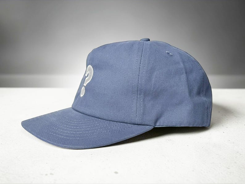 Custom embroidered question mark hat on blue cotton 5 panel snapback cap featuring structured crown and pre curved visor. Clean white embroidery symbol on front panel suitable for custom text, logo placement and daily wear. Adjustable snapback closure provides flexible fit with breathable cotton twill fabric. Product mockup shows front view on neutral background highlighting stitching detail, panel structure and consistent composition for all listing images.