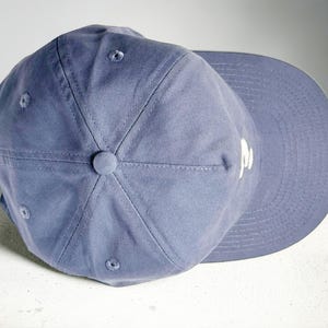 Custom embroidered question mark hat on blue cotton 5 panel snapback cap featuring structured crown and pre curved visor. Clean white embroidery symbol on front panel suitable for custom text, logo placement and daily wear. Adjustable snapback closure provides flexible fit with breathable cotton twill fabric. Product mockup shows front view on neutral background highlighting stitching detail, panel structure and consistent composition for all listing images.