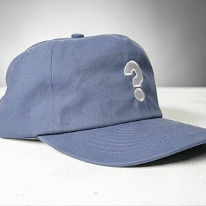 Custom embroidered question mark hat on blue cotton 5 panel snapback cap featuring structured crown and pre curved visor. Clean white embroidery symbol on front panel suitable for custom text, logo placement and daily wear. Adjustable snapback closure provides flexible fit with breathable cotton twill fabric. Product mockup shows front view on neutral background highlighting stitching detail, panel structure and consistent composition for all listing images.