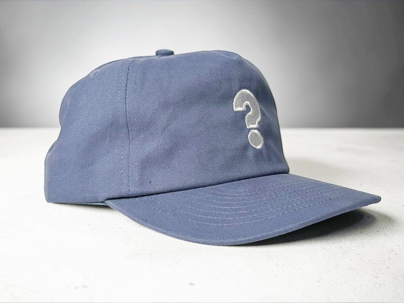 Custom embroidered question mark hat on blue cotton 5 panel snapback cap featuring structured crown and pre curved visor. Clean white embroidery symbol on front panel suitable for custom text, logo placement and daily wear. Adjustable snapback closure provides flexible fit with breathable cotton twill fabric. Product mockup shows front view on neutral background highlighting stitching detail, panel structure and consistent composition for all listing images.
