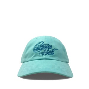 Custom embroidered script hat with personalized text on teal cotton twill dad cap featuring unstructured low profile shape and adjustable strap closure. Clean stitched lettering design on front panel suitable for branding, custom text display and everyday wear. Soft breathable cotton fabric with curved visor and detailed embroidery finish.