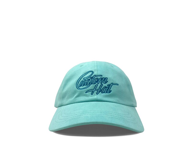 Custom embroidered script hat with personalized text on teal cotton twill dad cap featuring unstructured low profile shape and adjustable strap closure. Clean stitched lettering design on front panel suitable for branding, custom text display and everyday wear. Soft breathable cotton fabric with curved visor and detailed embroidery finish.